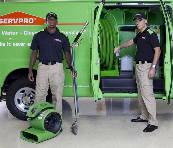 Two guys standing by a green van with green equipment.